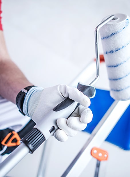 Peintre avec rouleau à peinture : préparation travaux Gros plan sur la main d'un peintre portant un gant blanc, tenant fermement le manche d'un rouleau à peinture neuf, en préparation d'une rénovation.