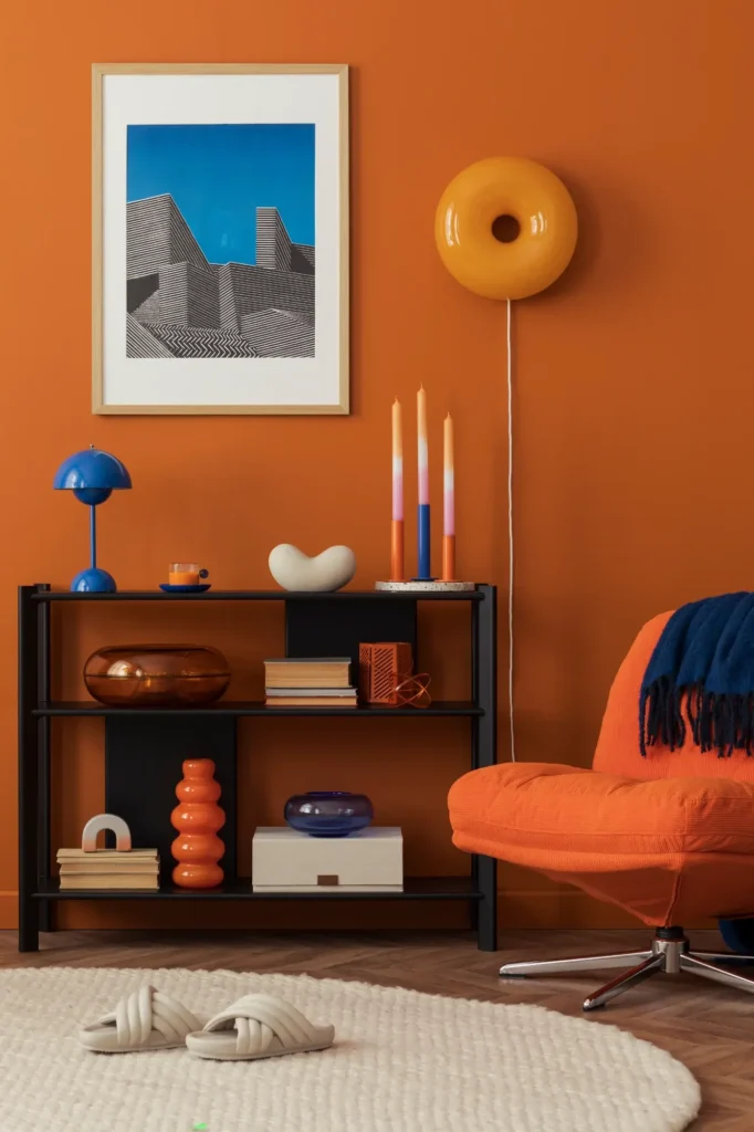 Salon vibrant : Déco moderne orange brûlé et touches de bleu. Salon moderne orange brûlé : étagère noire remplie d'objets colorés, fauteuil orange, lampe donut murale jaune et tableau graphique bleu.